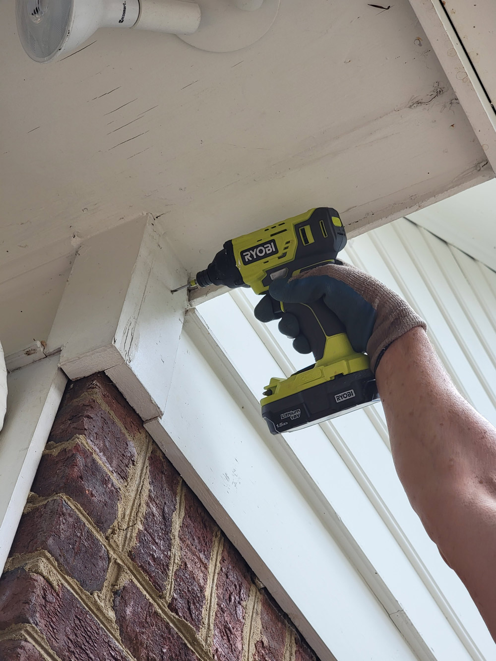 A man using a Ryobi drill to drill into wood on a house.