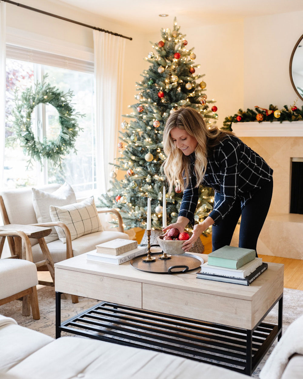Woman placing bowl on table with Christmas Tree and holiday wreath in the background