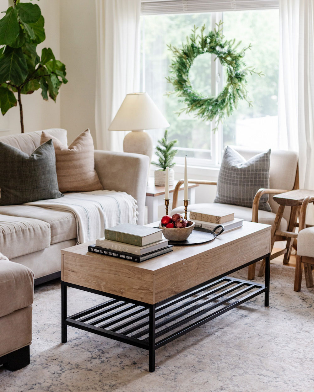Center shot of a coffee table with beige furniture around it and a holiday wreath placed in the back window