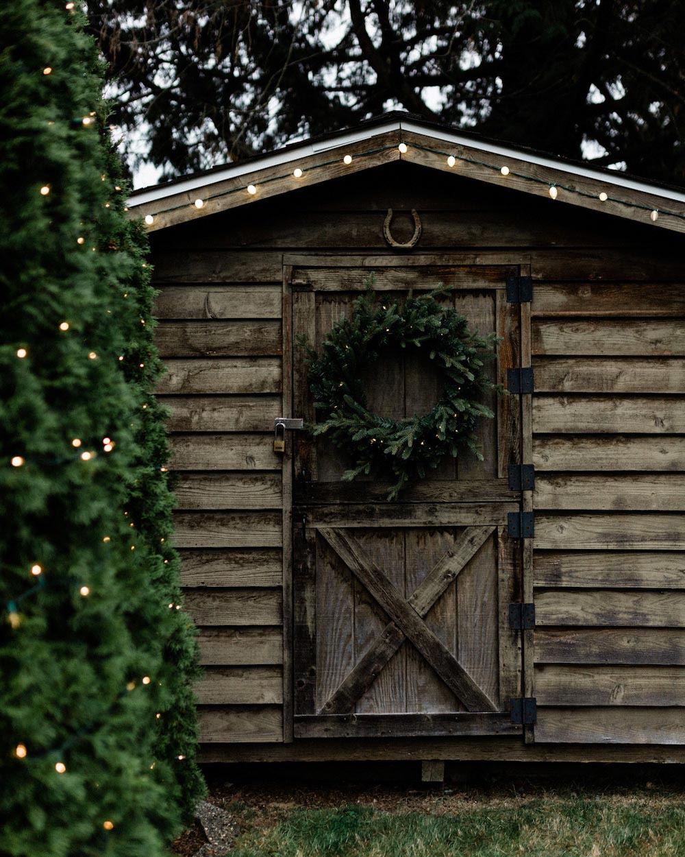 Wooden shed with wreath on the front door with string lights hanging from the roof