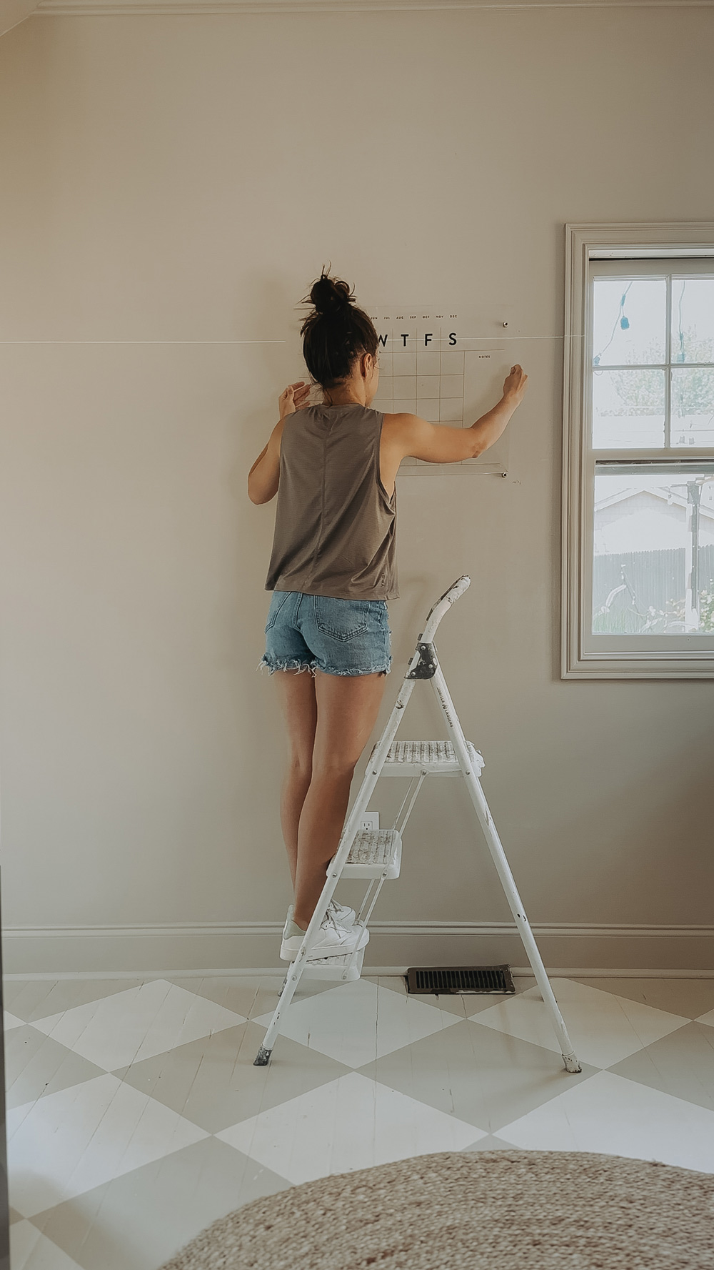 A person using a step stool to hang up a calendar.