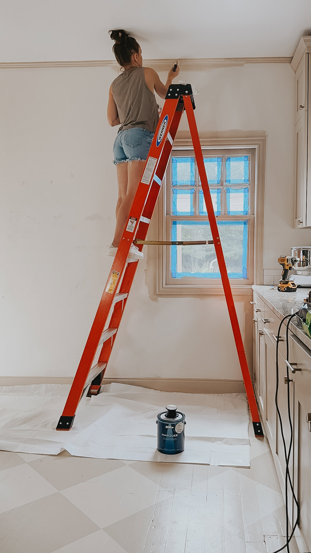 A person on a ladder painting a wall.