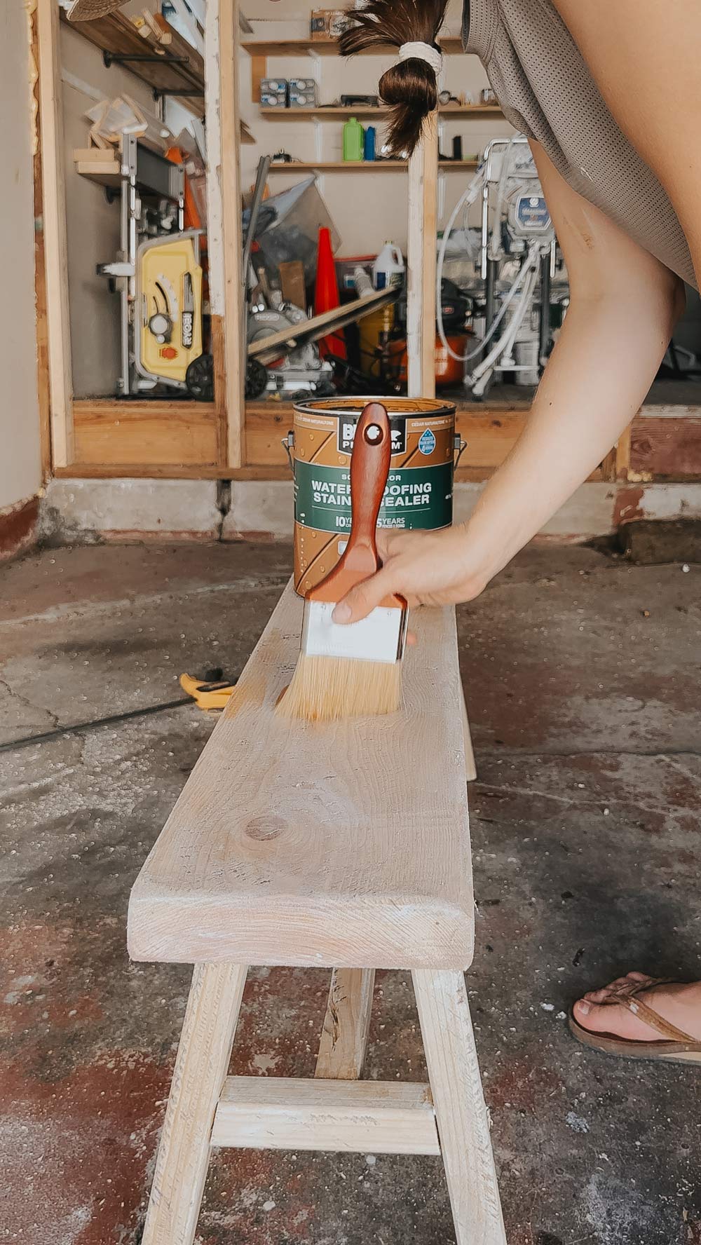 A person adding stain and sealer to a bench.