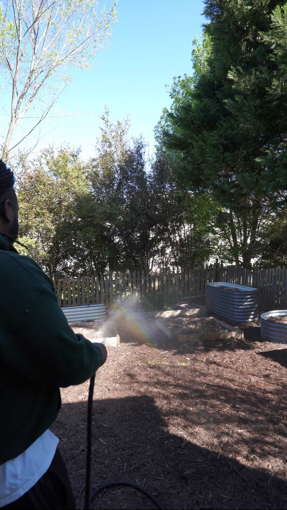 Man using a water hose to spray freshly laid mulch.