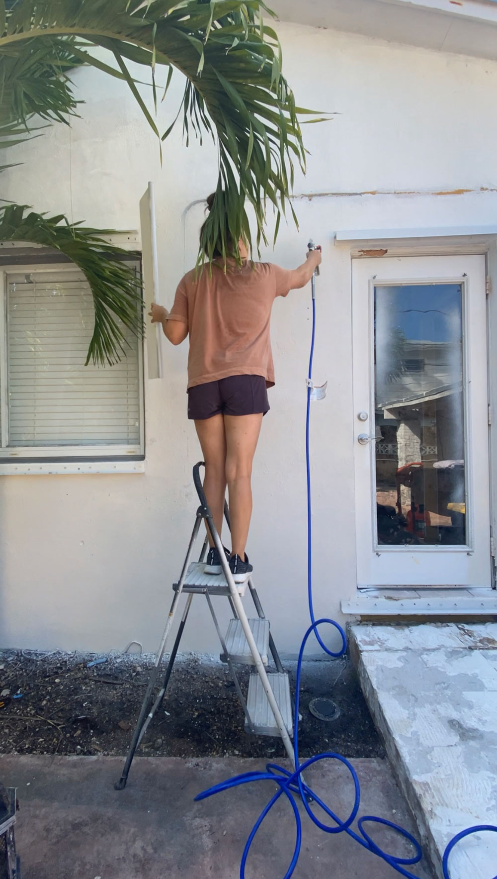 A woman on a ladder spraying paint on an exterior wall. A woman on a ladder spraying paint on an exterior wall.