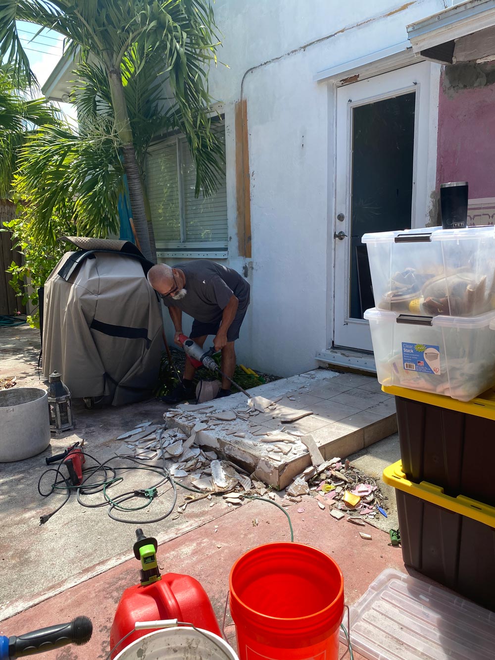 A man lifting tile from a step near an exterior door. A man lifting tile from a step near an exterior door.