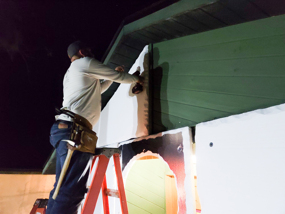 A man on a ladder attaching an insulation board to a house.