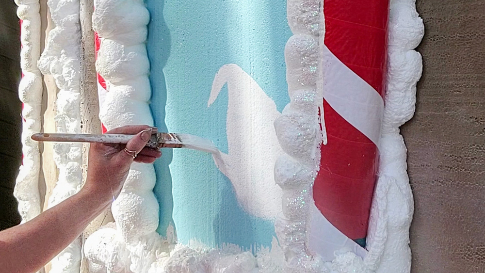 A hand painting details on a Life-Sized Gingerbread house.