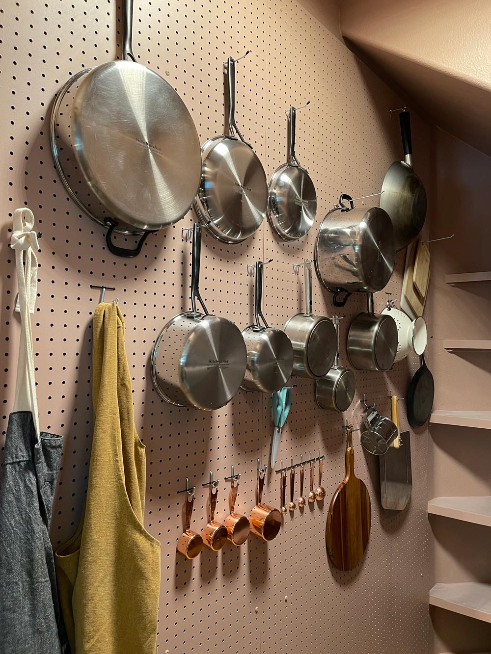 Pots, pans, aprons, and measuring cups on the pegboard wall. 