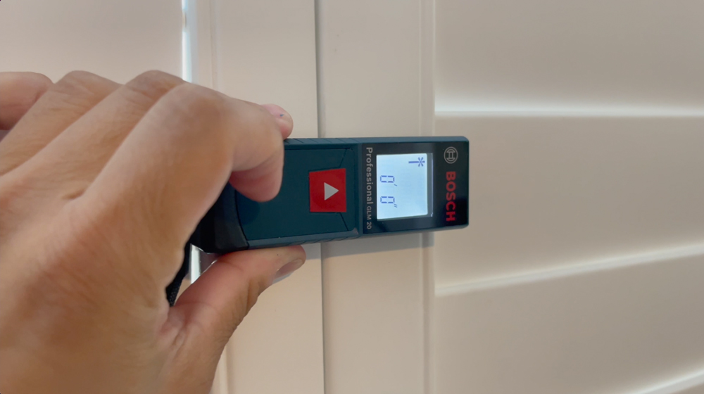 Close up of a Bosch Laser Measuring Tool being held to a wall. Close up of a Bosch Laser Measuring Tool being held to a wall.