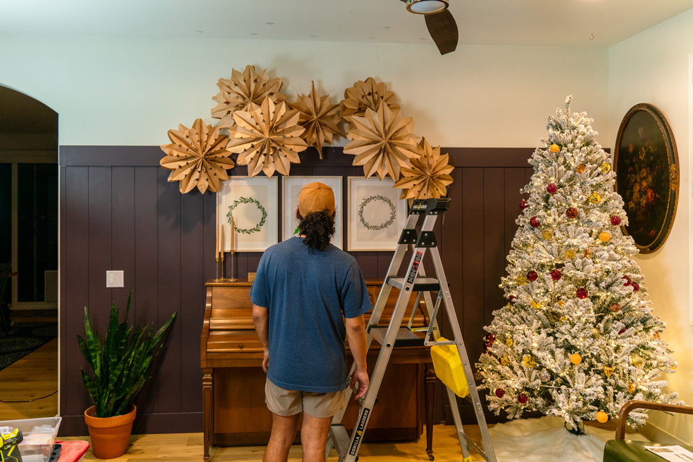 A man standing next to a ladder looking at styled DIY paper bag snowflakes. A man standing next to a ladder looking at styled DIY paper bag snowflakes.