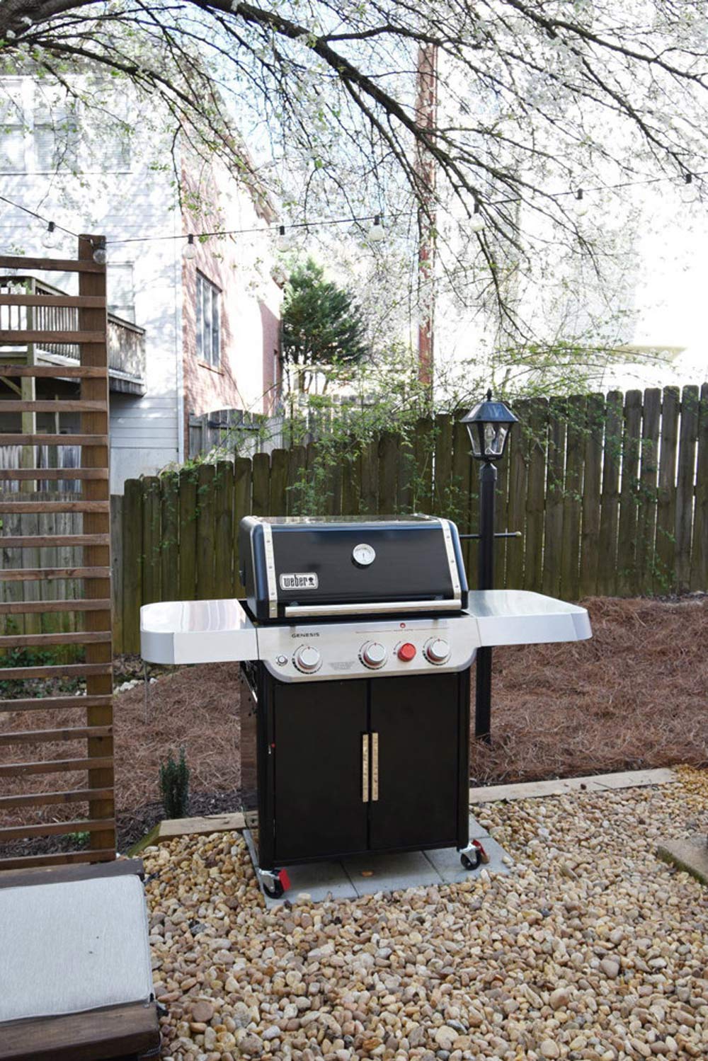 Black grill in fenced backyard next to solar pole outdoor light.