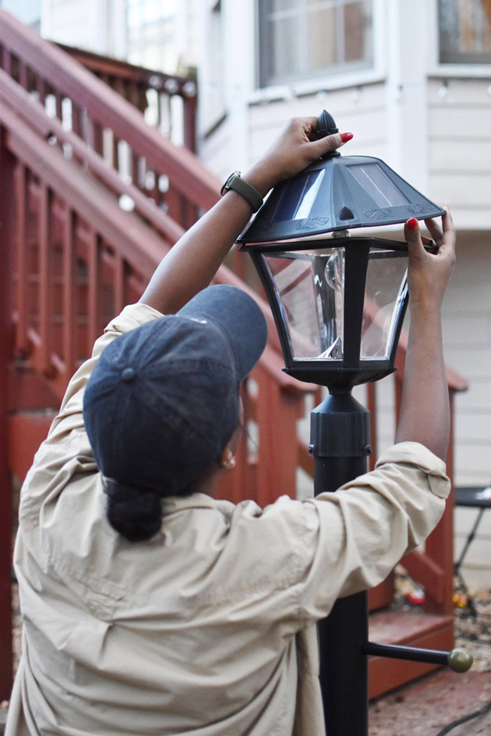 Woman in black baseball hat adjusting black covered outdoor stand pole solar light.