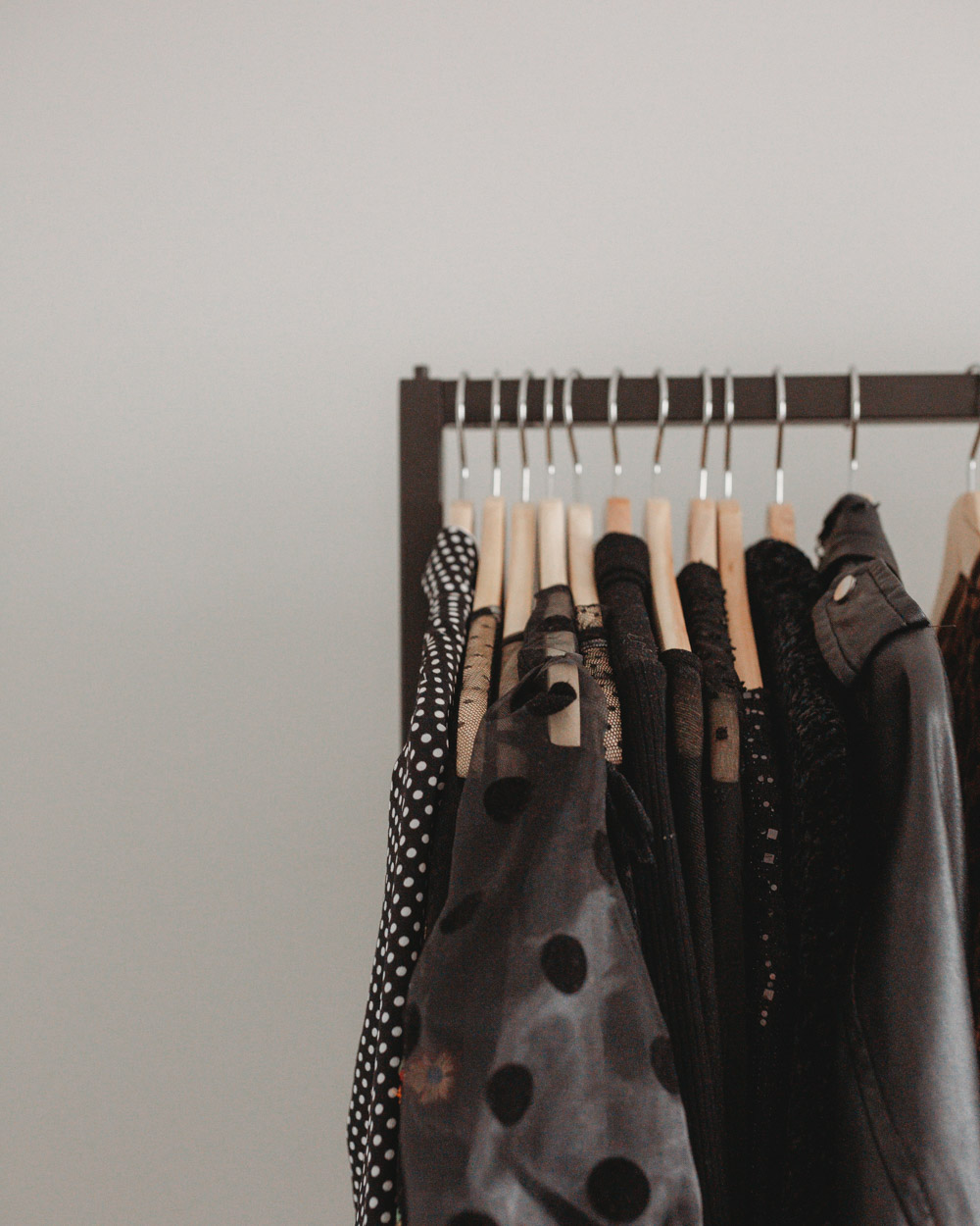 A close up view of a modern clothing rack with dark clothing on wooden hangers.