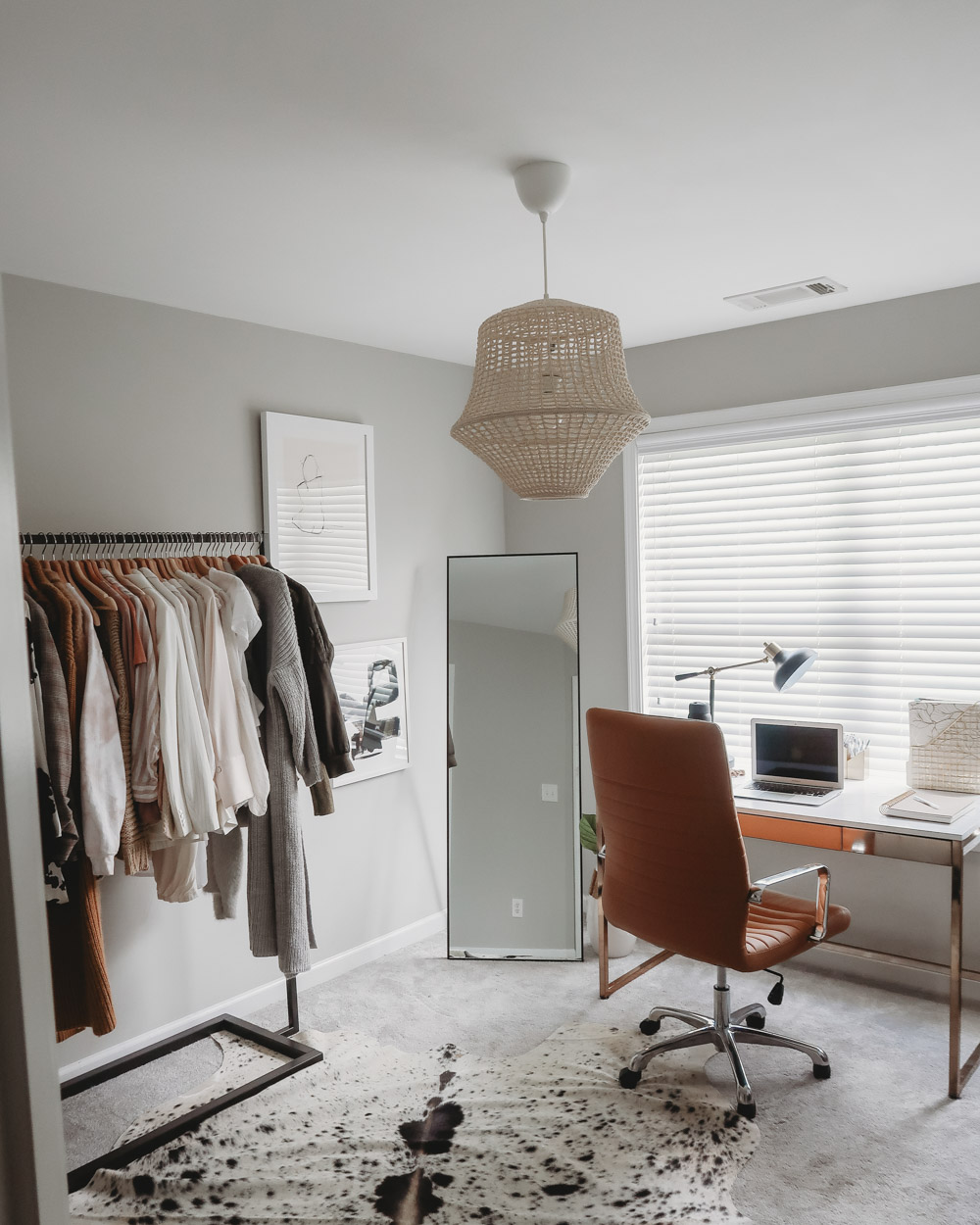 A room with an updated desk, clothing rack, and cowhide rug.