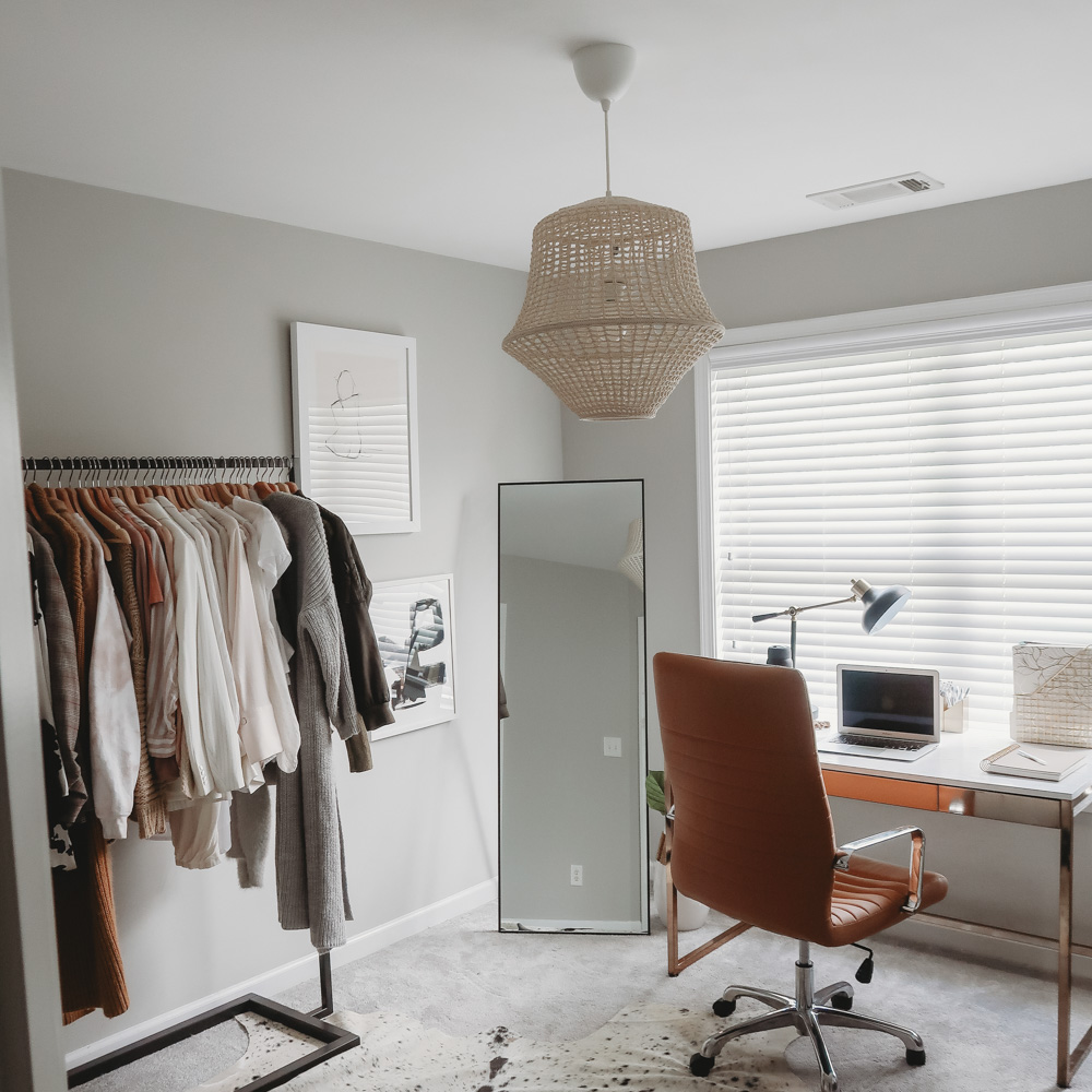 An office with a desk, full length mirror, and clothing rack.