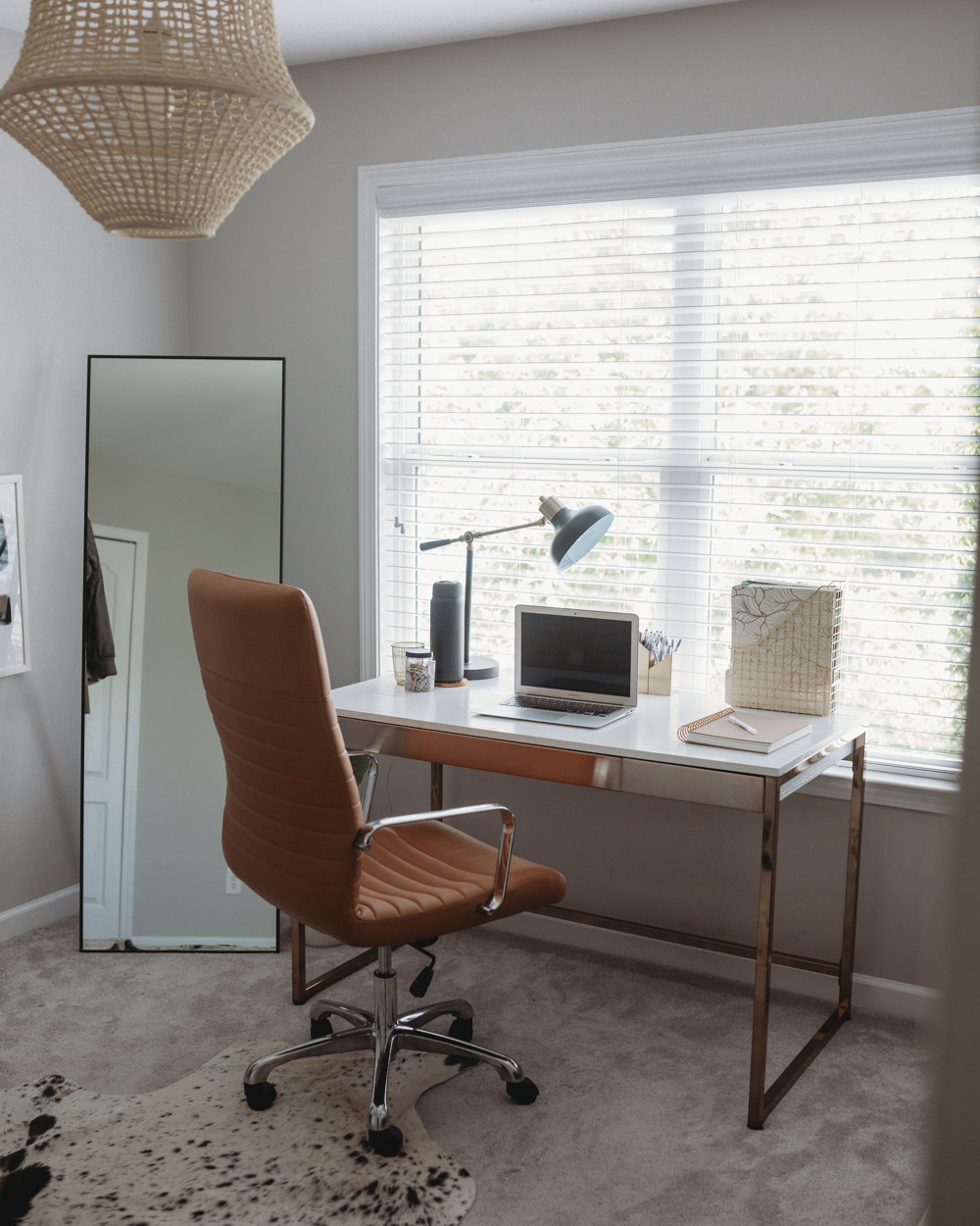 A window with a modern desk and tan leather chair in front of it.