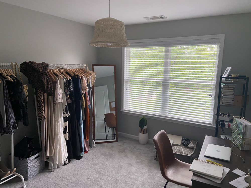 A room being used as an office and closet with a desk and clothing racks.
