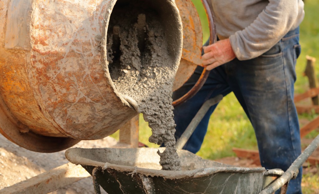 A Pro pours concrete from a mixer to a wheelbarrow.