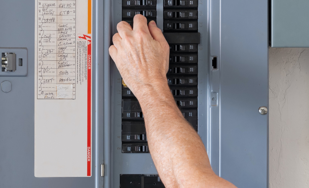 A person adjusts a circuit breaker on an electrical panel.