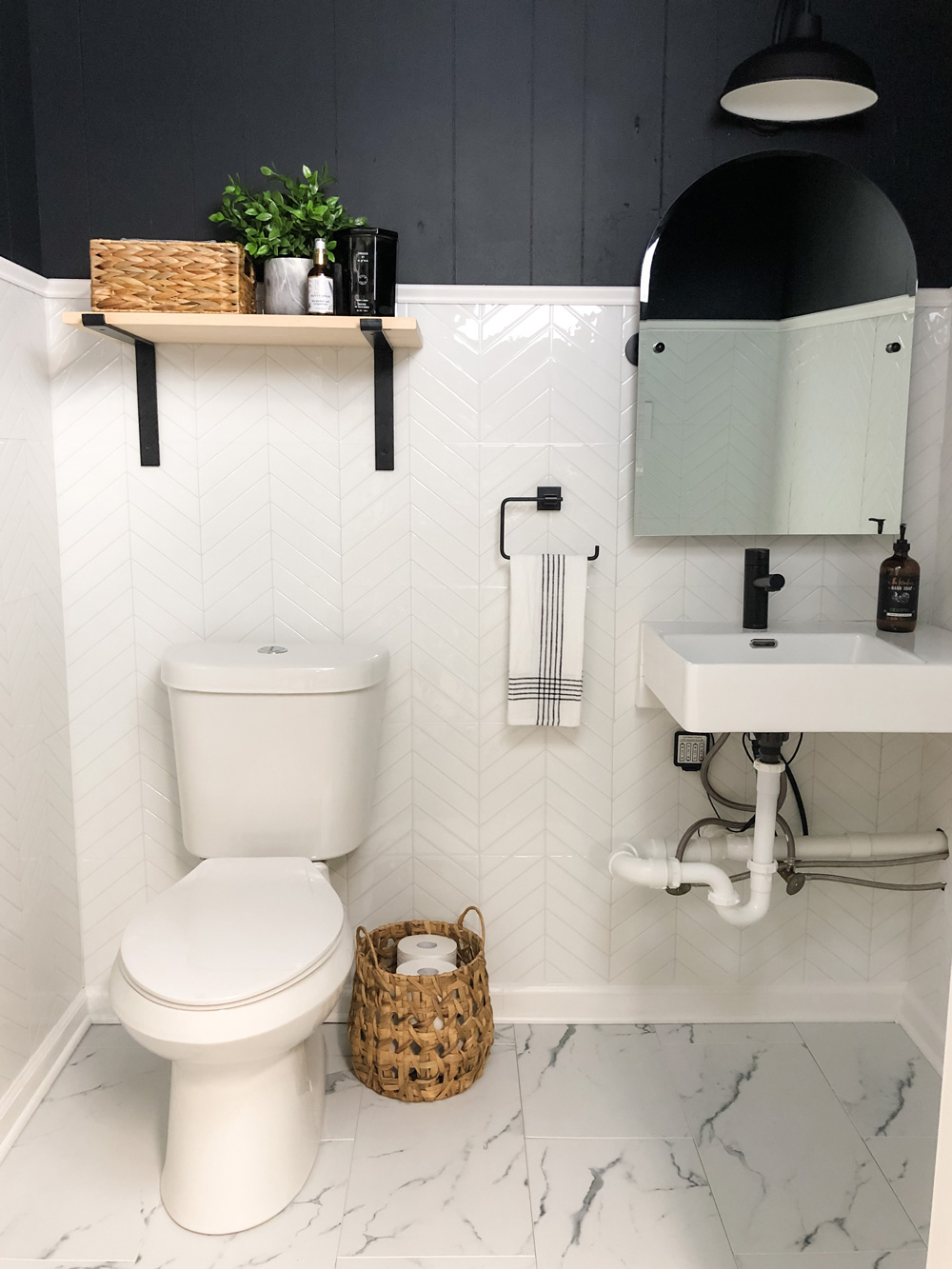Finished bathroom featuring black shiplap and white tile on walls and marble tile on floors.