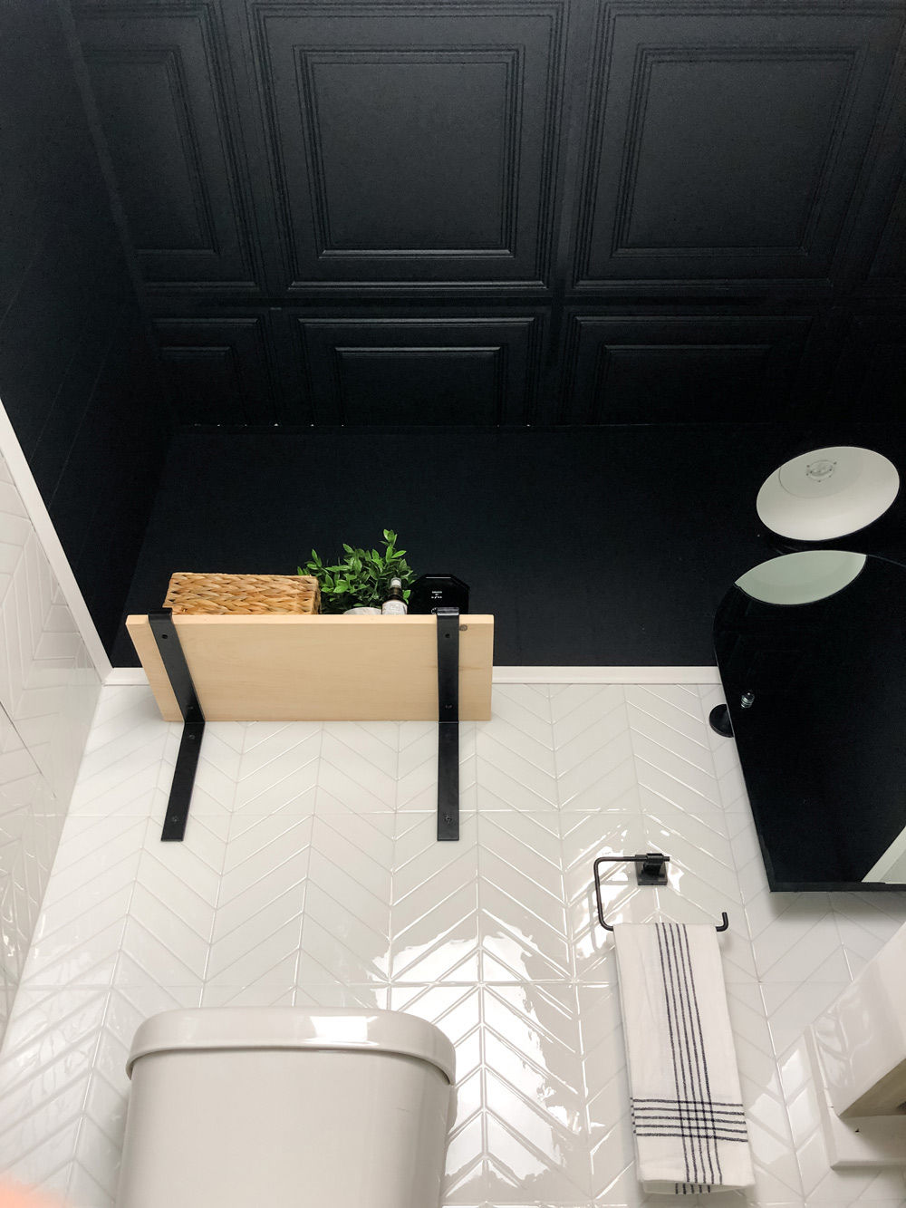 Black decorative ceiling tiles featured above wooden shelf and toilet.