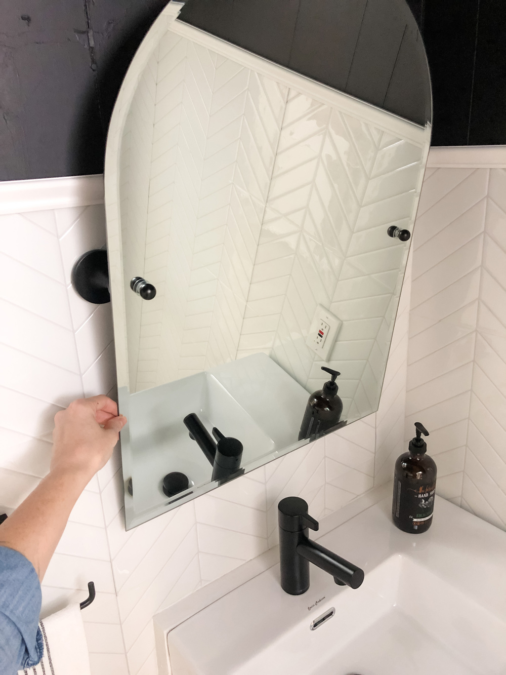 Hand touching tiltable mirror featured in bathroom.