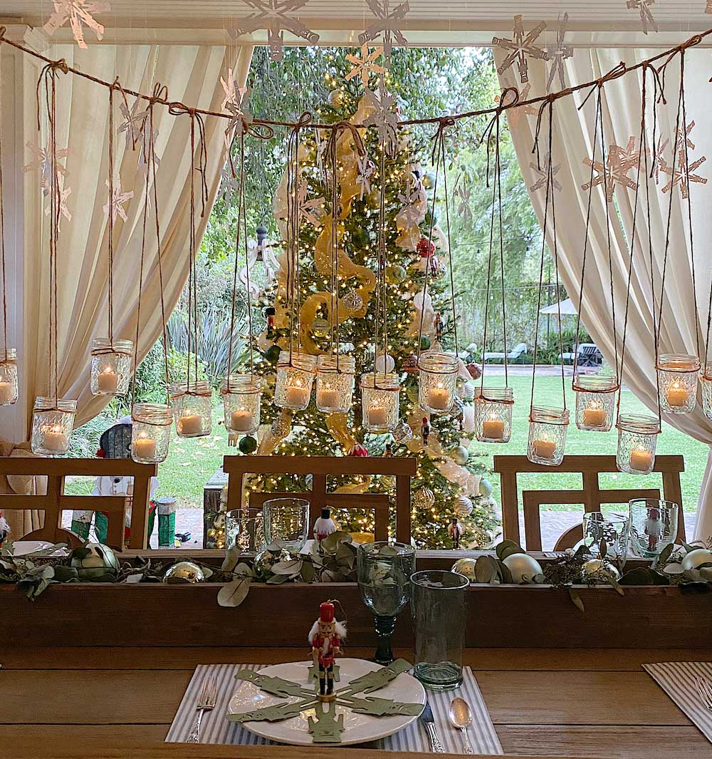 Table styled with holiday decor, hanging votive candles and a Christmas tree in the background
