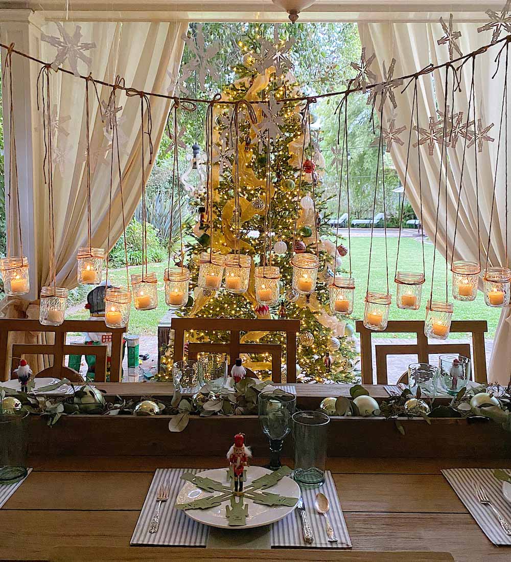 Table styled with holiday decor, hanging votive candles and a Christmas tree in the background
