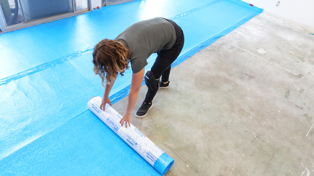 A woman rolling flooring liner out on a concrete floor.