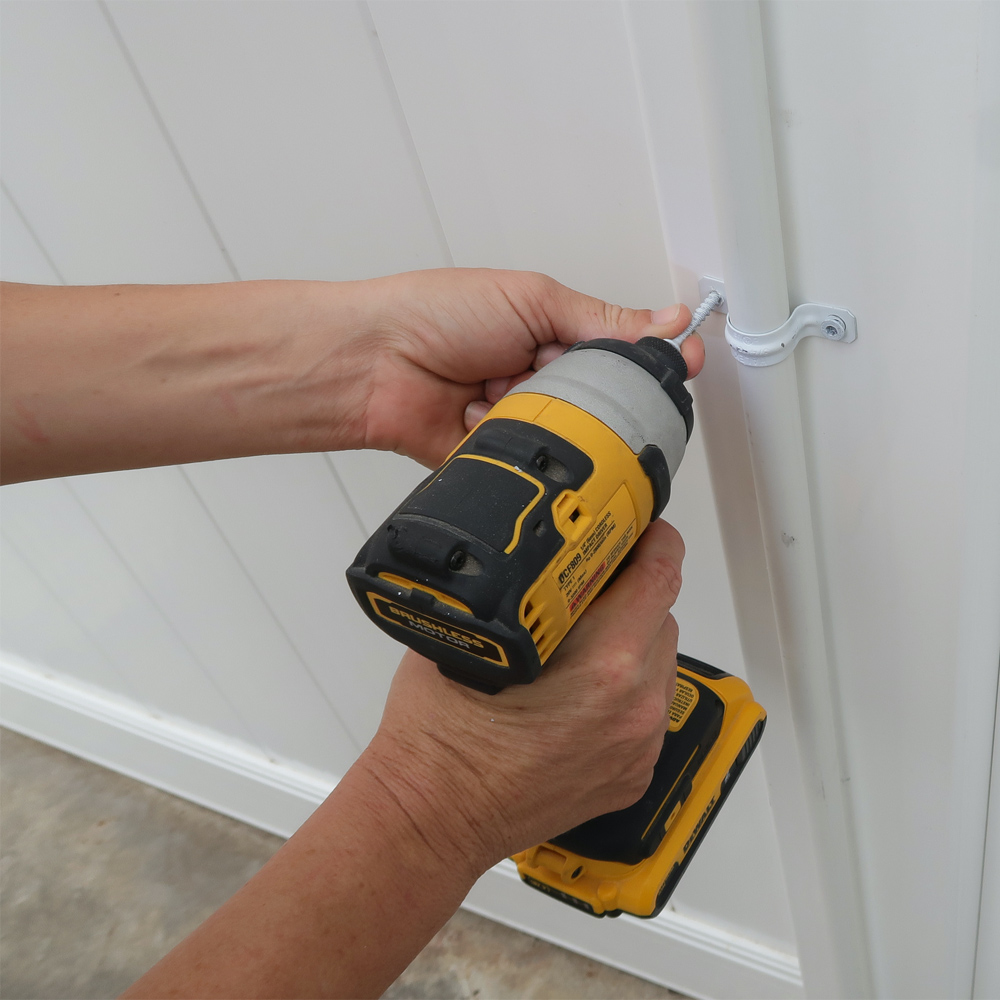 Person drilling  fencer topper to fence with screws and conduit straps.