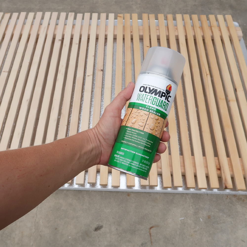 Person holding wood sealer spray in front of wood structure.