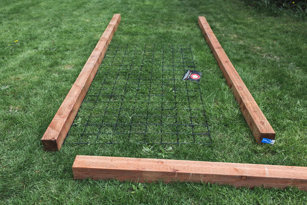 Medium stain columns of wood laid on grass in a rectangle with black square wire in the middle.