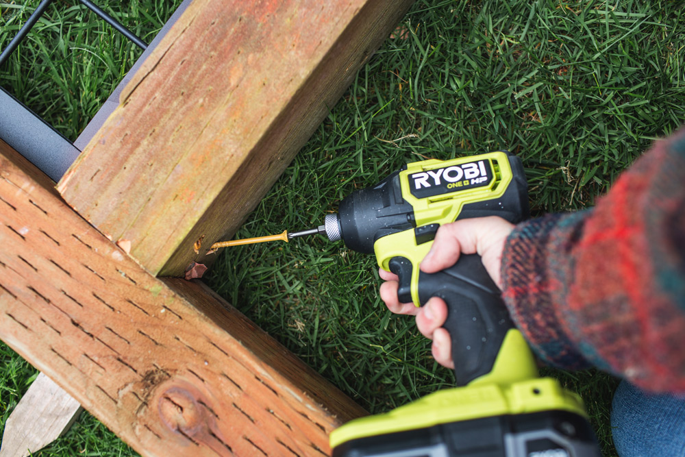 Close up of woman drilling two pieces of trellis together at corners with Ryobi drill.