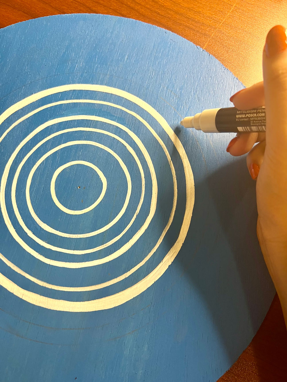 Person using a Posca marker to paint white circles on a wooden circle.