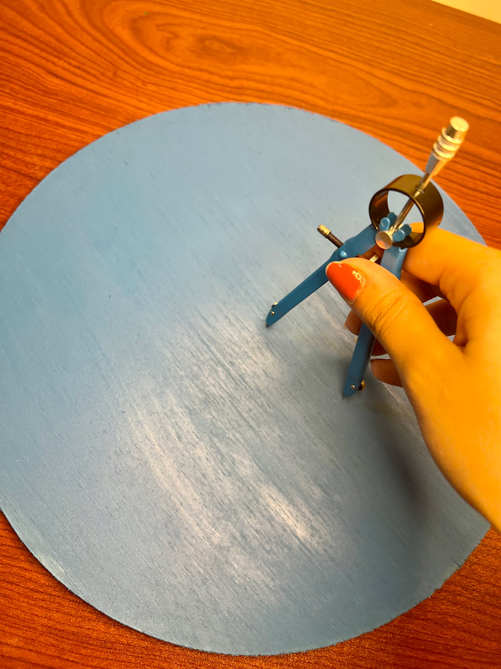 Person using a protractor to create a circle on a blue wooden circle.