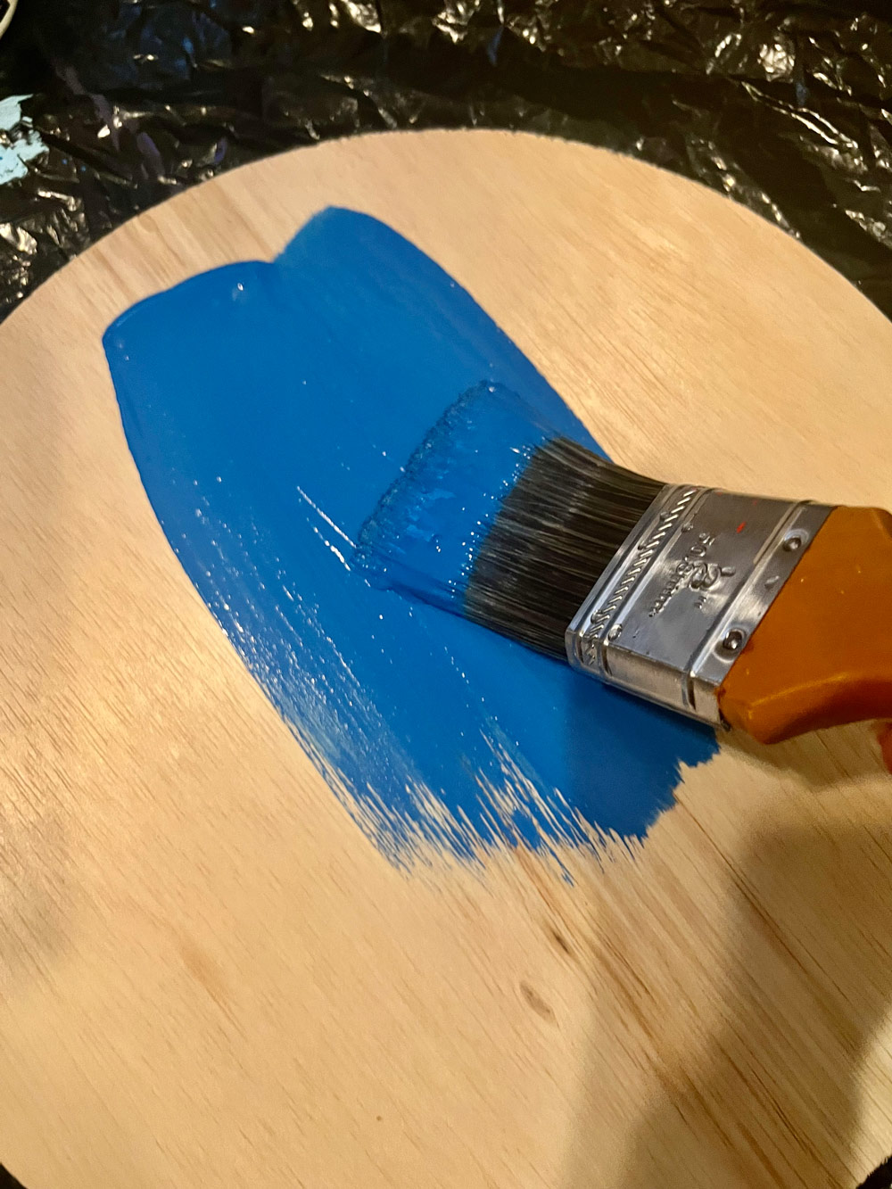A wooden circle being painted blue with a paintbrush.