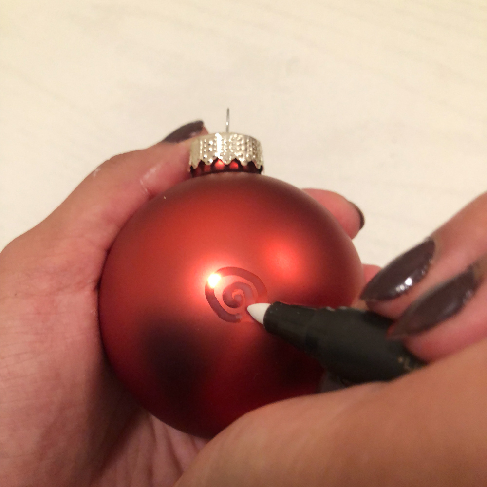 Person using a marker to draw a swirl on a holiday ornament.