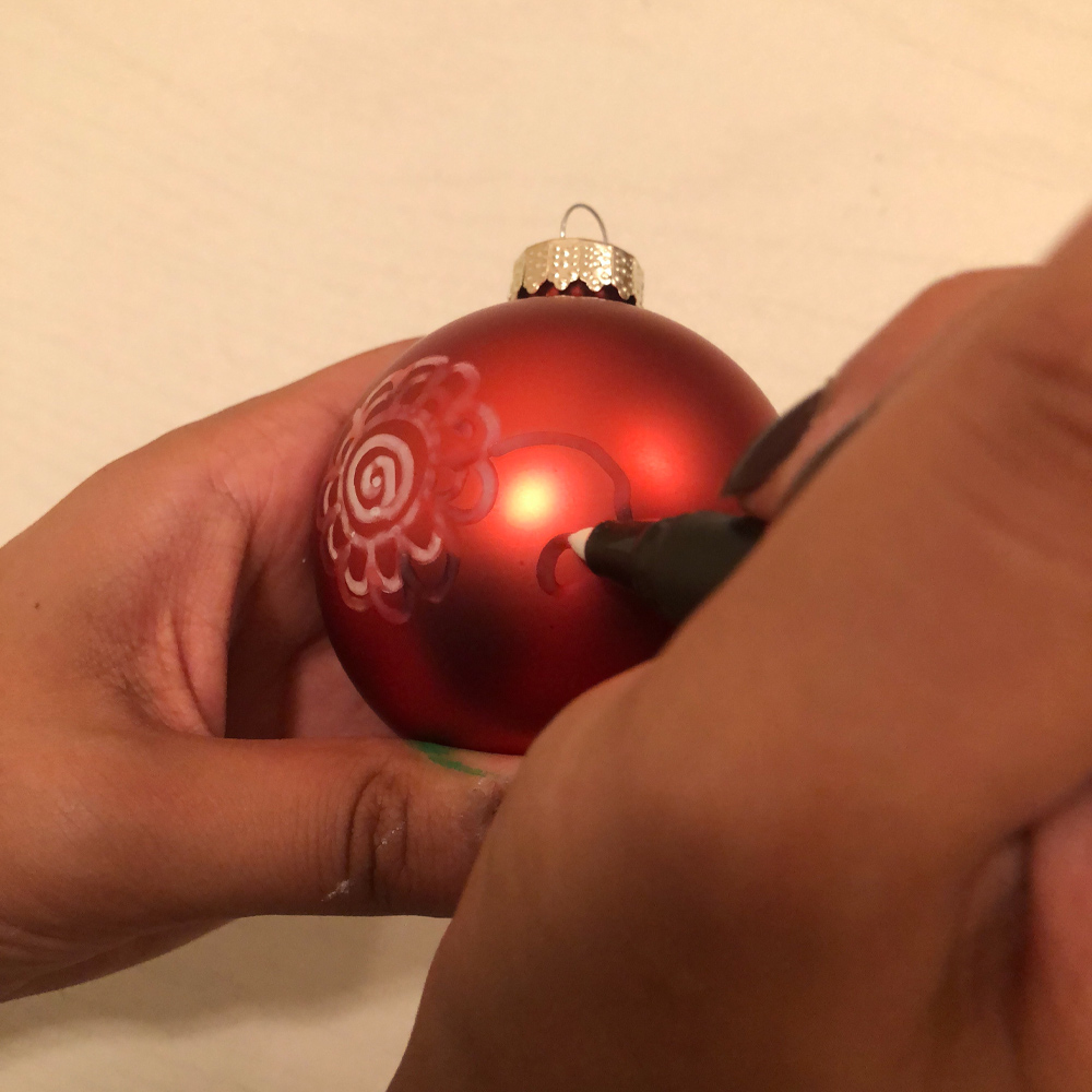 Person using a marker to draw paisleys on a holiday ornament.