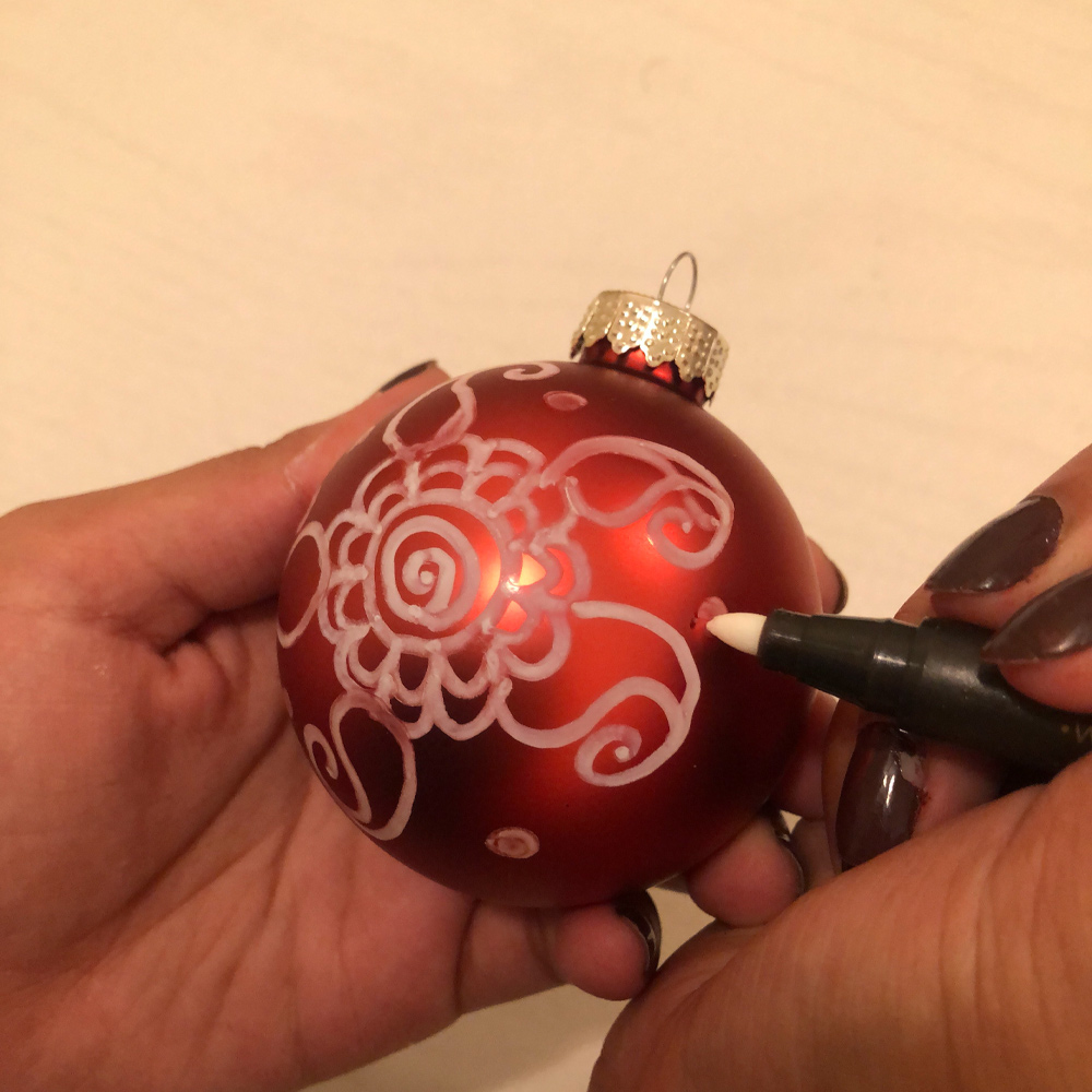 Person using a marker to draw dots on a holiday ornament.