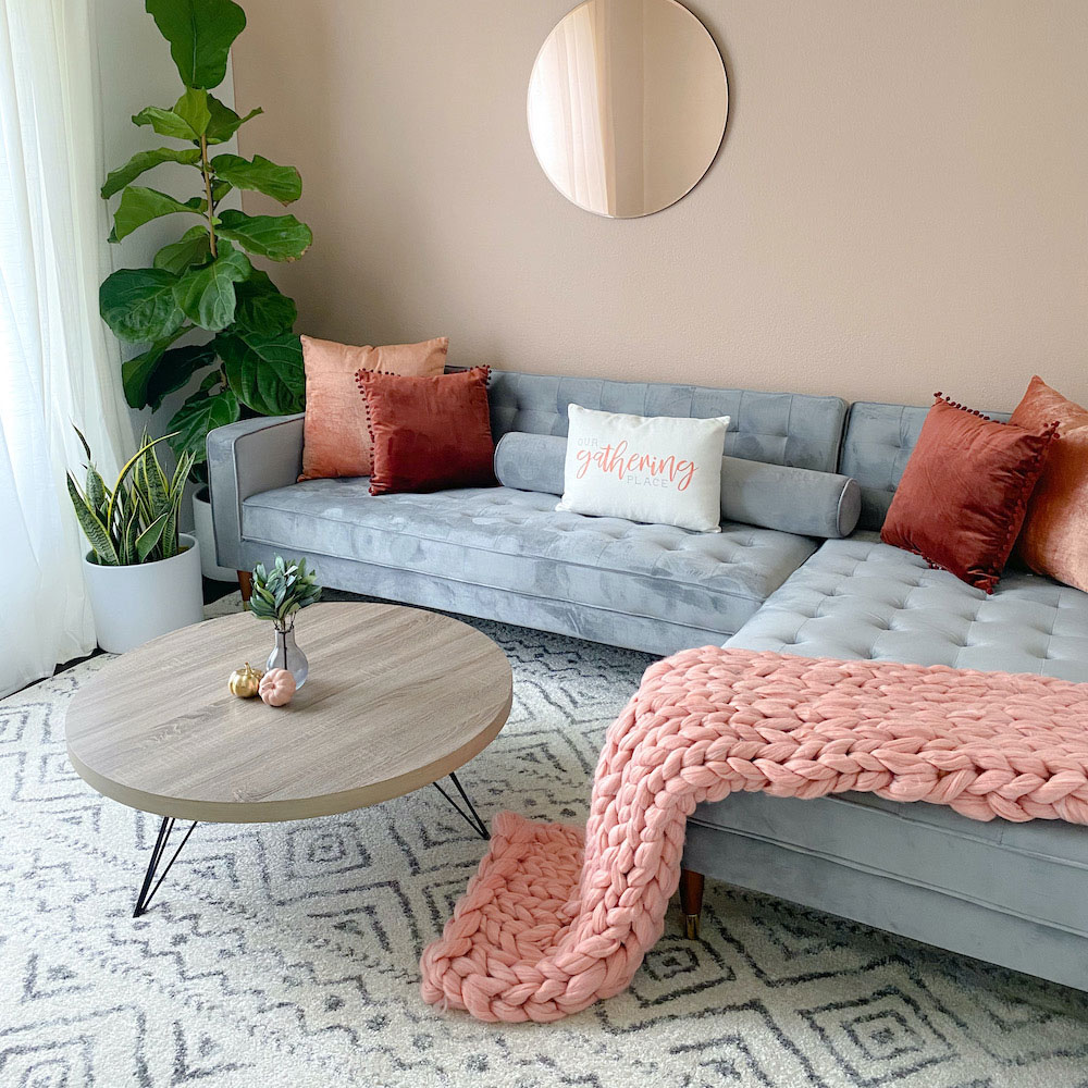 A living room with light pink walls and a light gray sectional sofa.