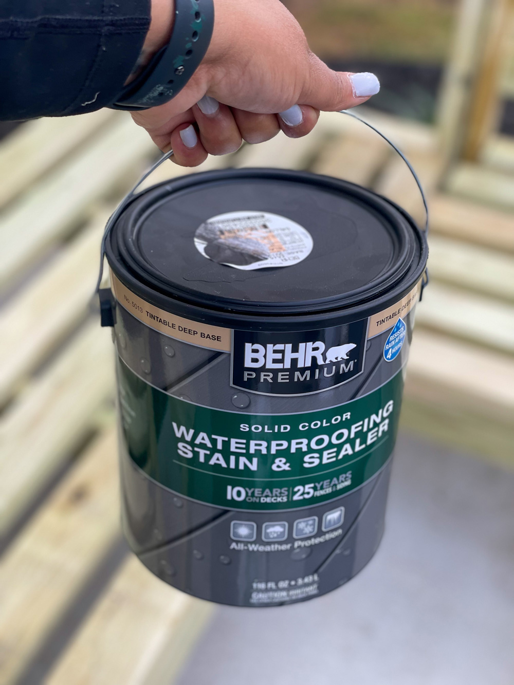 Person holding a can of Behr Premium Waterproofing Stain and Sealer. Person holding a can of Behr Premium Waterproofing Stain and Sealer.