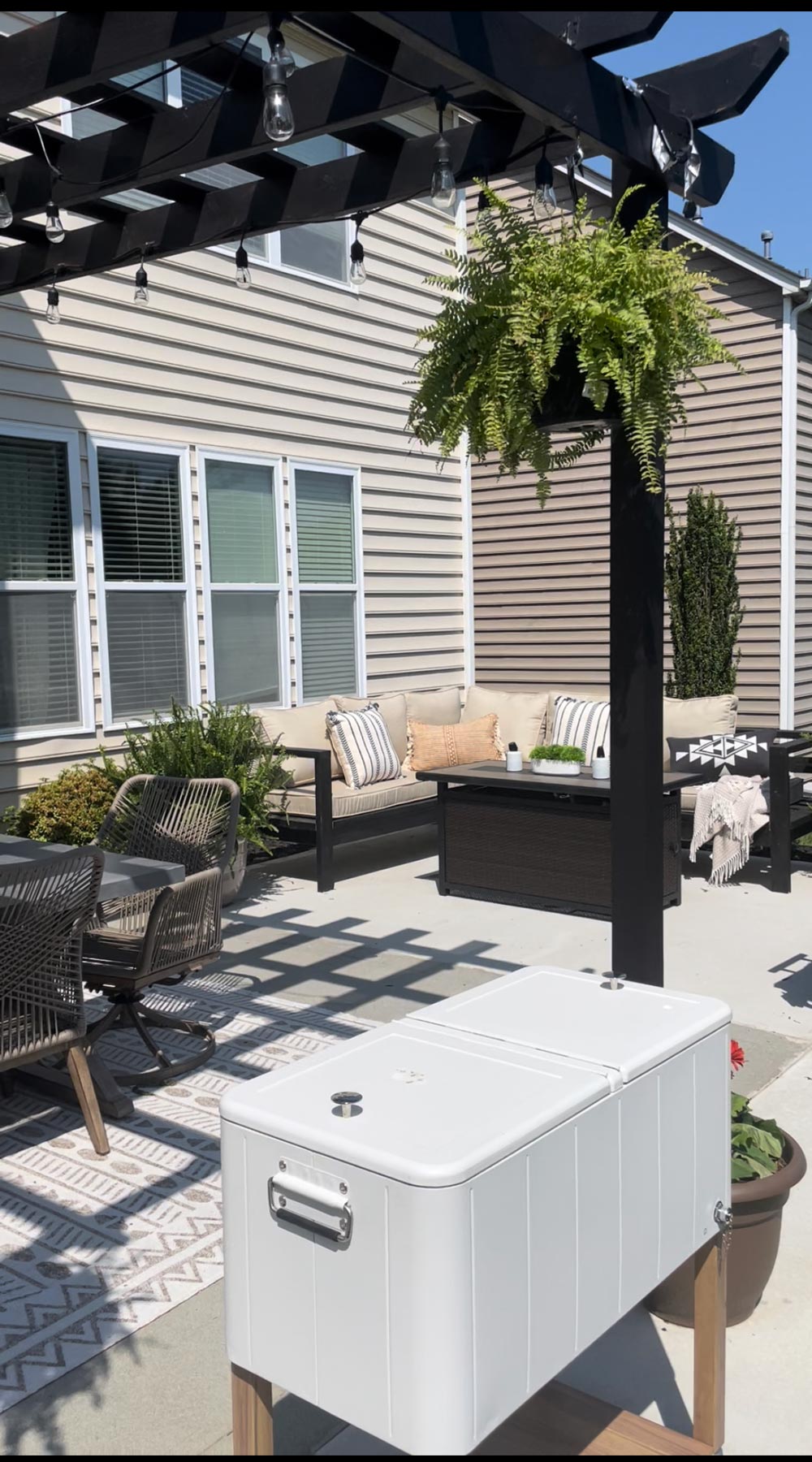 Backyard area with a hanging fern, table with chairs, and an outdoor couch with pillows. Backyard area with a hanging fern, table with chairs, and an outdoor couch with pillows.