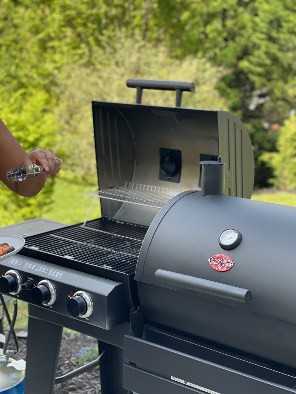 Two grills and a person holding a pair of tongs. Two grills and a person holding a pair of tongs.