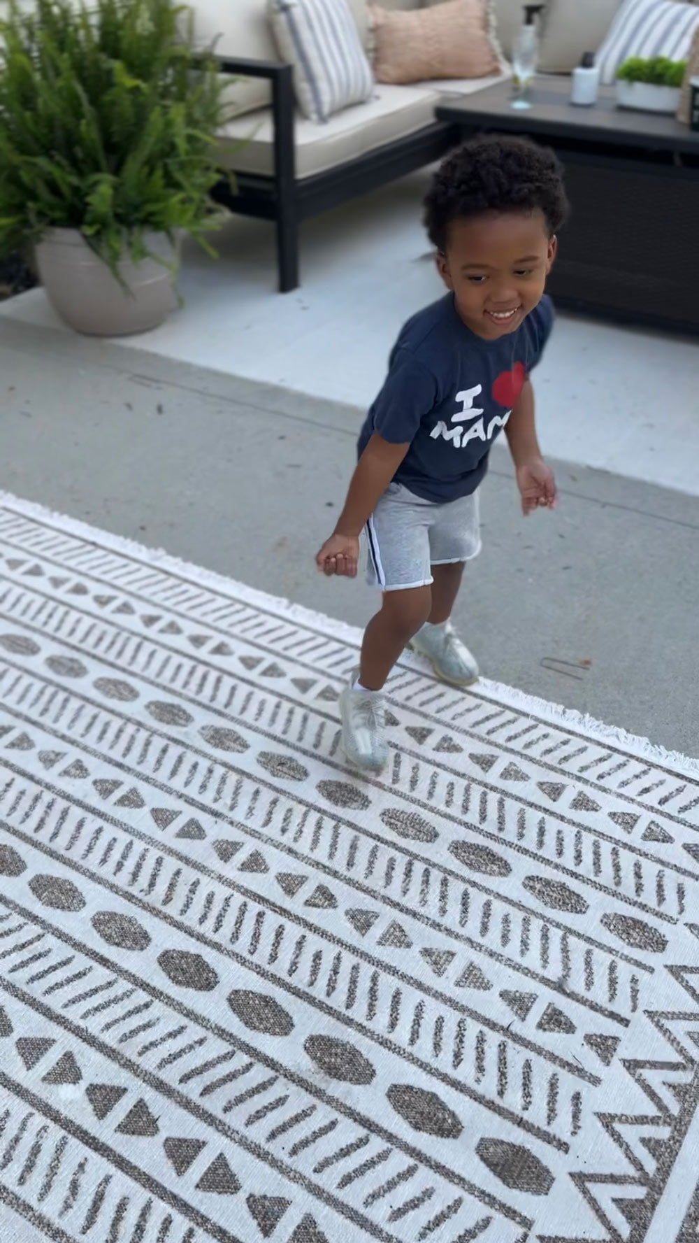 A boy smiling and standing on top of a patterned rug. A boy smiling and standing on top of a patterned rug.