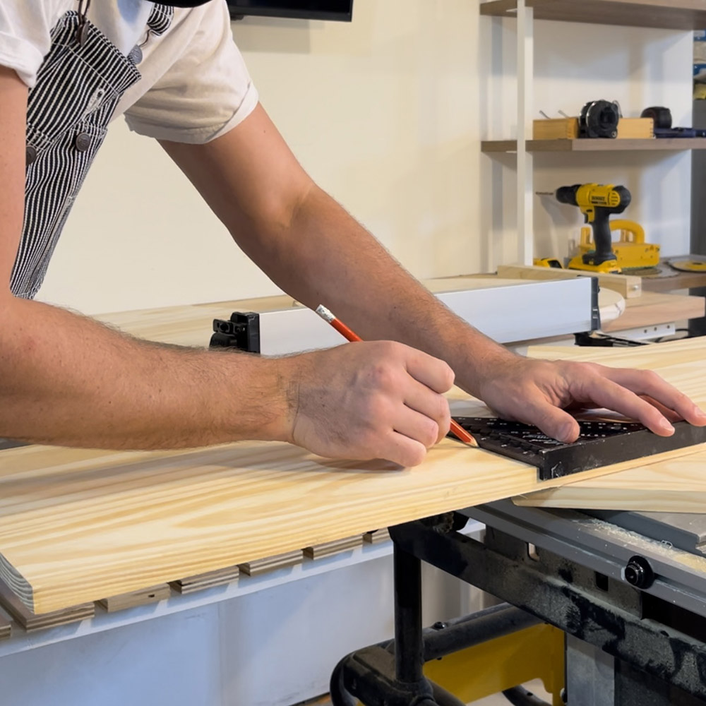 A man drawing a line on a piece of wood using a ruler and pencil.