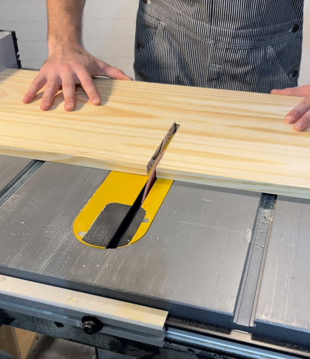 A man cutting a small rectangle out of a plank of wood using a miter saw.