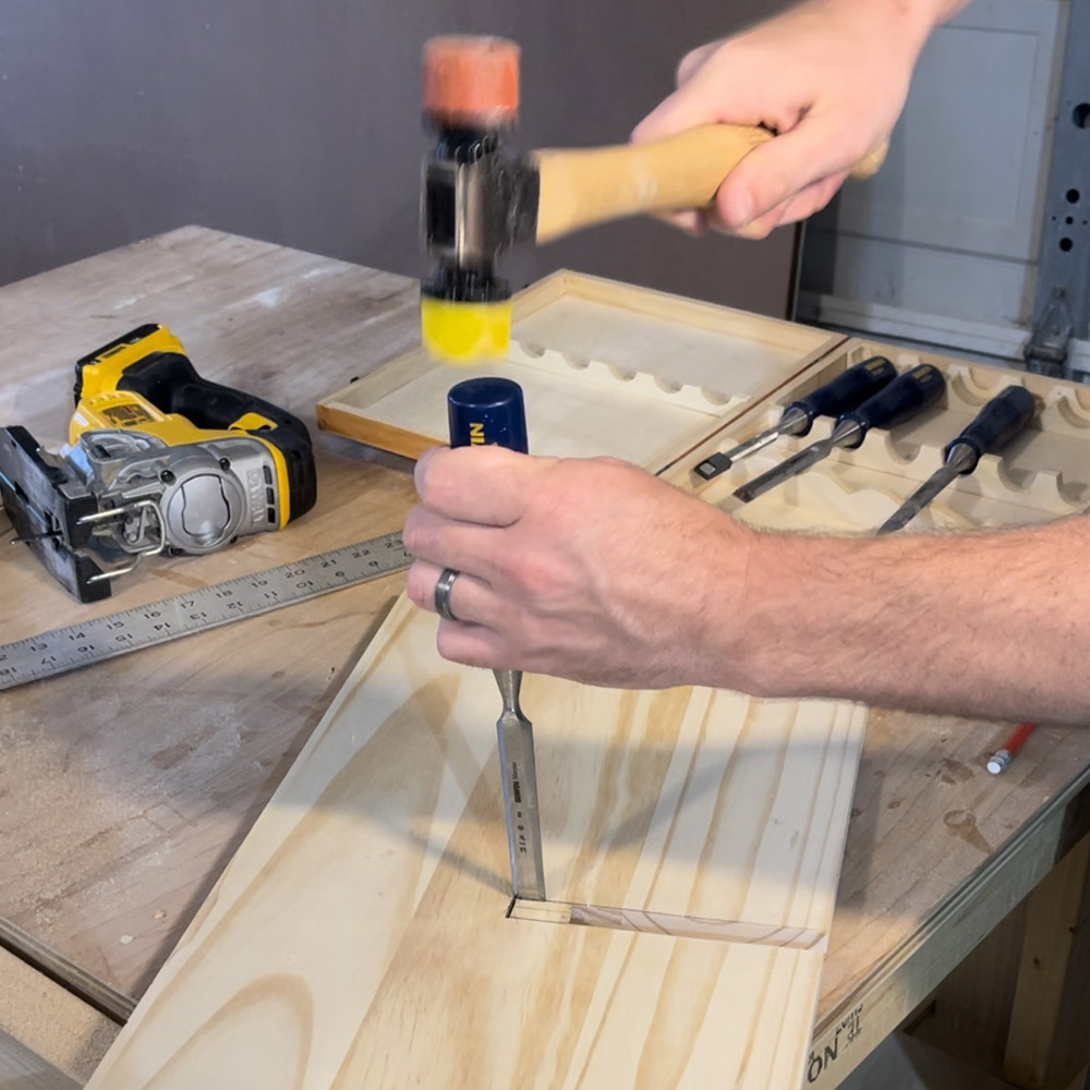 A man using a jigsaw and chisel to knock a small rectangle out of a piece of wood.