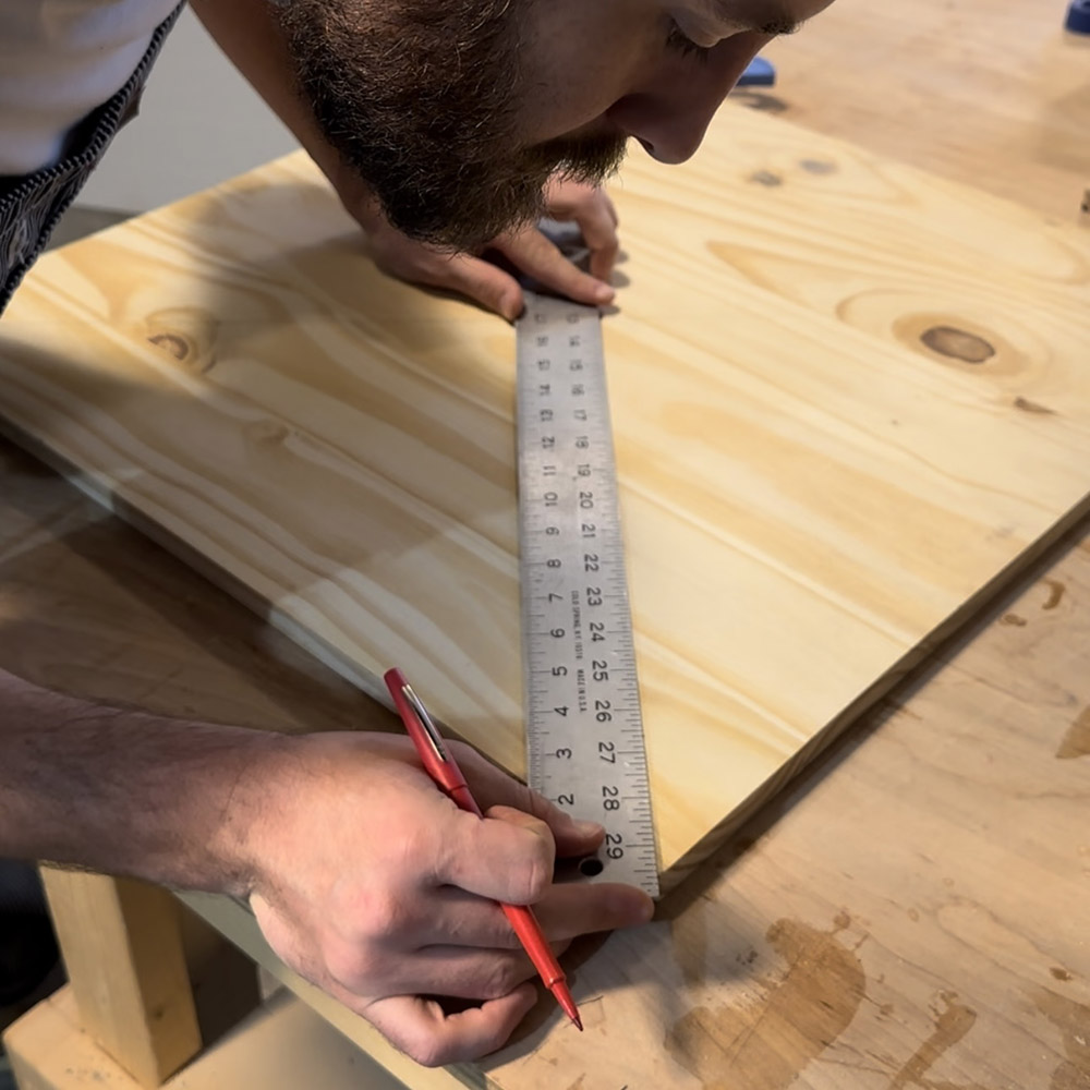 A man measuring a piece of wood with a ruler.