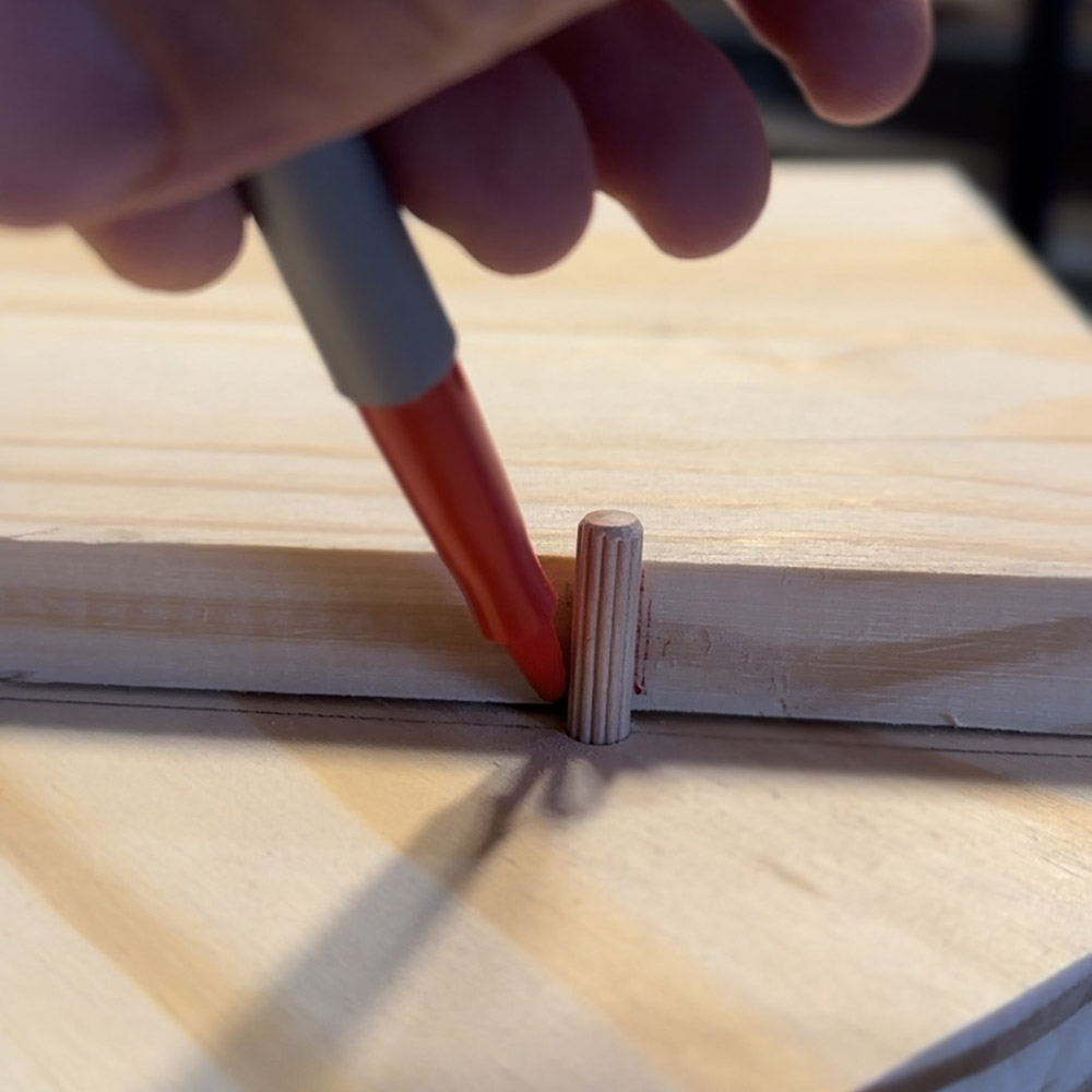 A man marking dowels connected to a wooden plank with a marker.